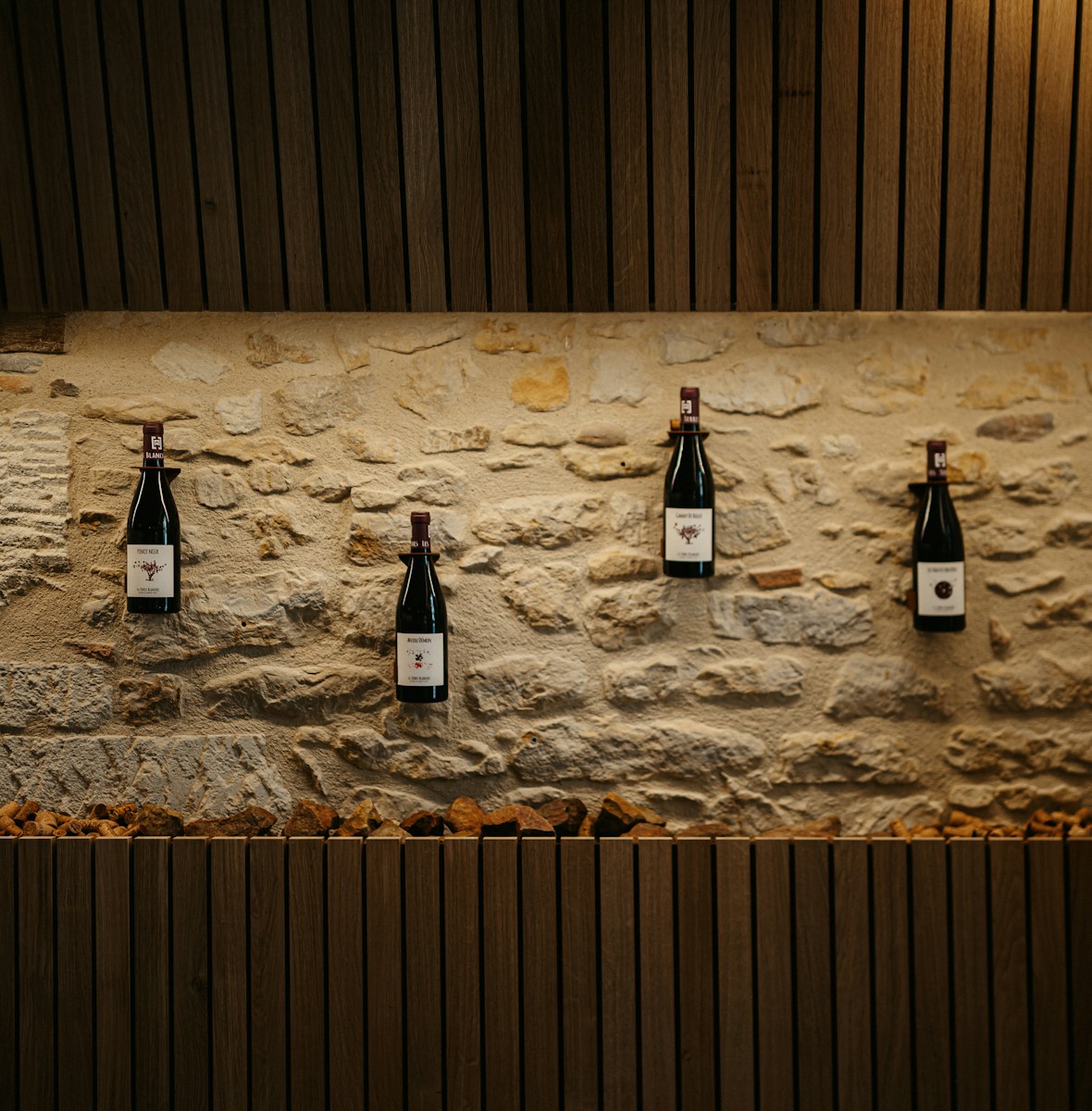 four bottles of wine are hanging on a stone wall